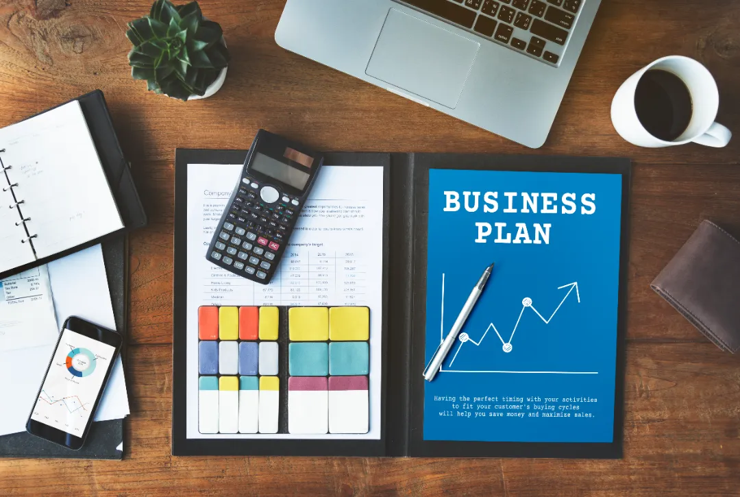 Workspace with business plan documents, laptop, and financial tools for mailbox rental planning