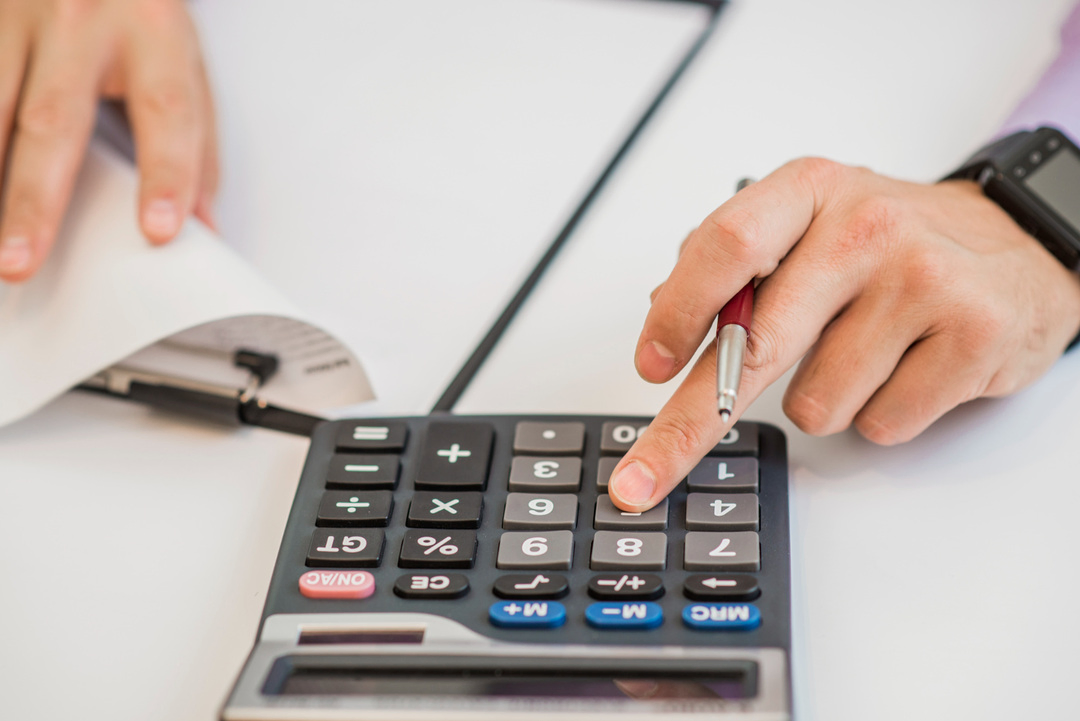 Hands holding pen and calculator, symbolizing competitive price setting.